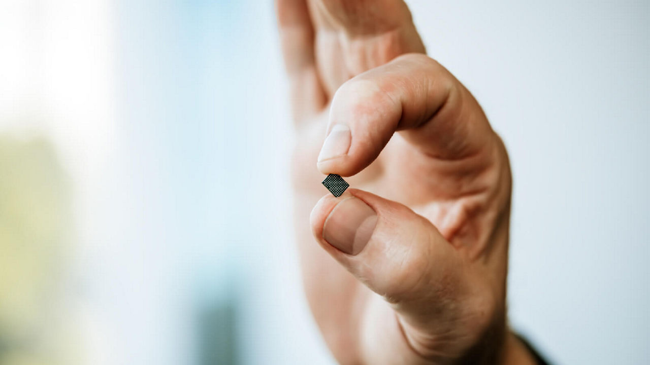Hand holding modern microchip with grid pattern – innovative technology on blurred blue and beige background