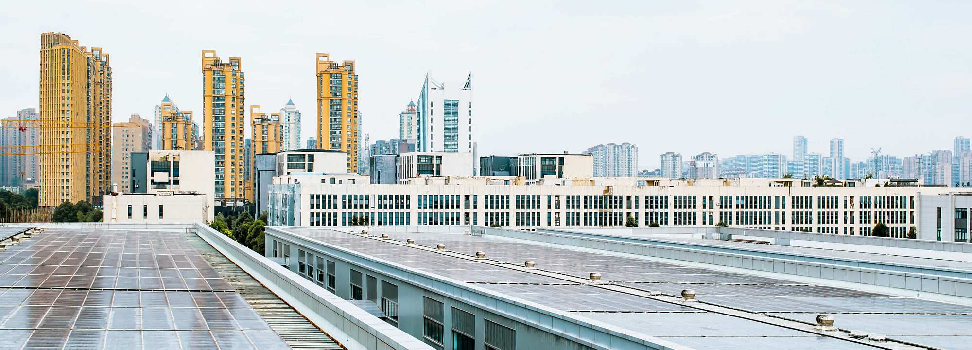 Rooftop view of industrial buildings with solar panels in Hefei, China, with modern high-rise buildings and city skyline in the background under a bright, overcast sky