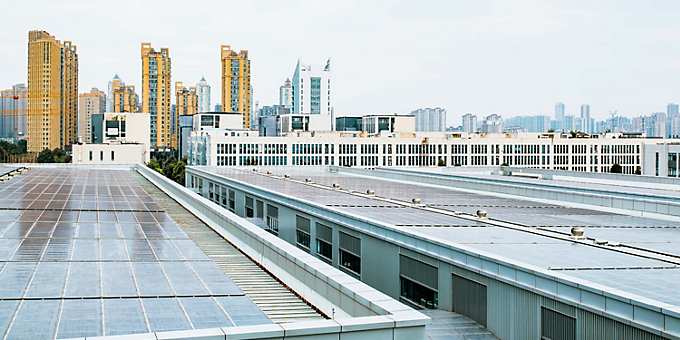 Rooftop view of industrial buildings with solar panels in Hefei, China, with modern high-rise buildings and city skyline in the background under a bright, overcast sky