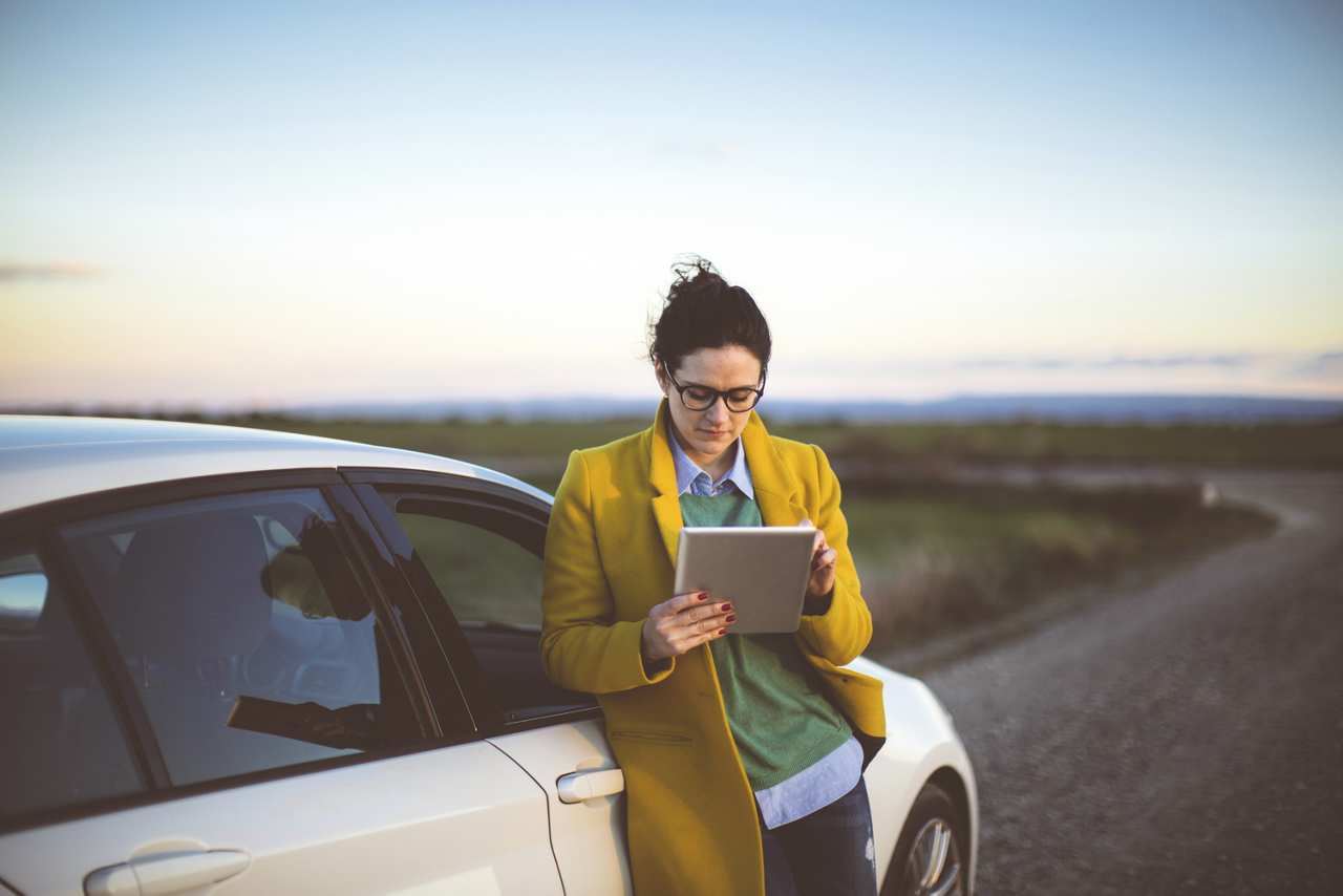 A woman with tablet in front of car